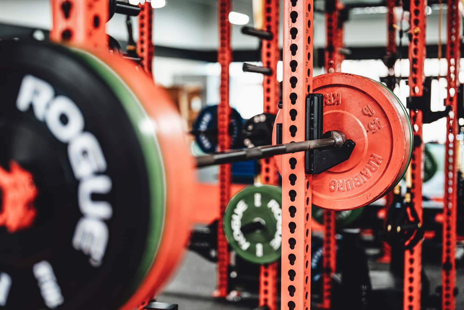 A home garage gym with a loaded barbell, weight plates and a steel power rack